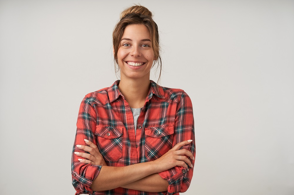 Young pretty female with bun hairstyle wearing casual clothes, looking happily to camera with crossed arms on chest