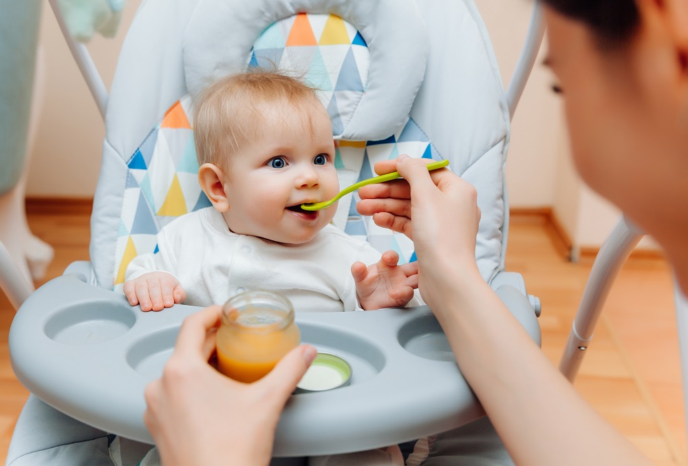 Mother gives fruit sauce to baby.mom feeds baby on highchair.baby food